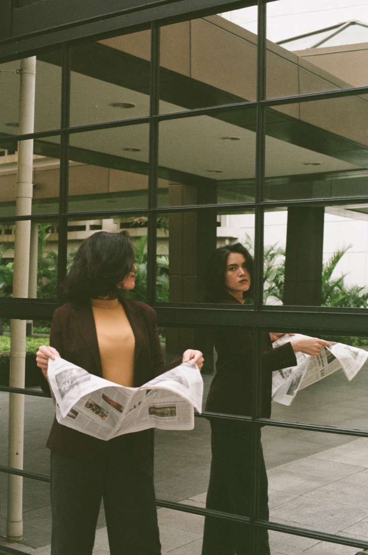 Filananda reading a newspaper, reflected in a glass facade